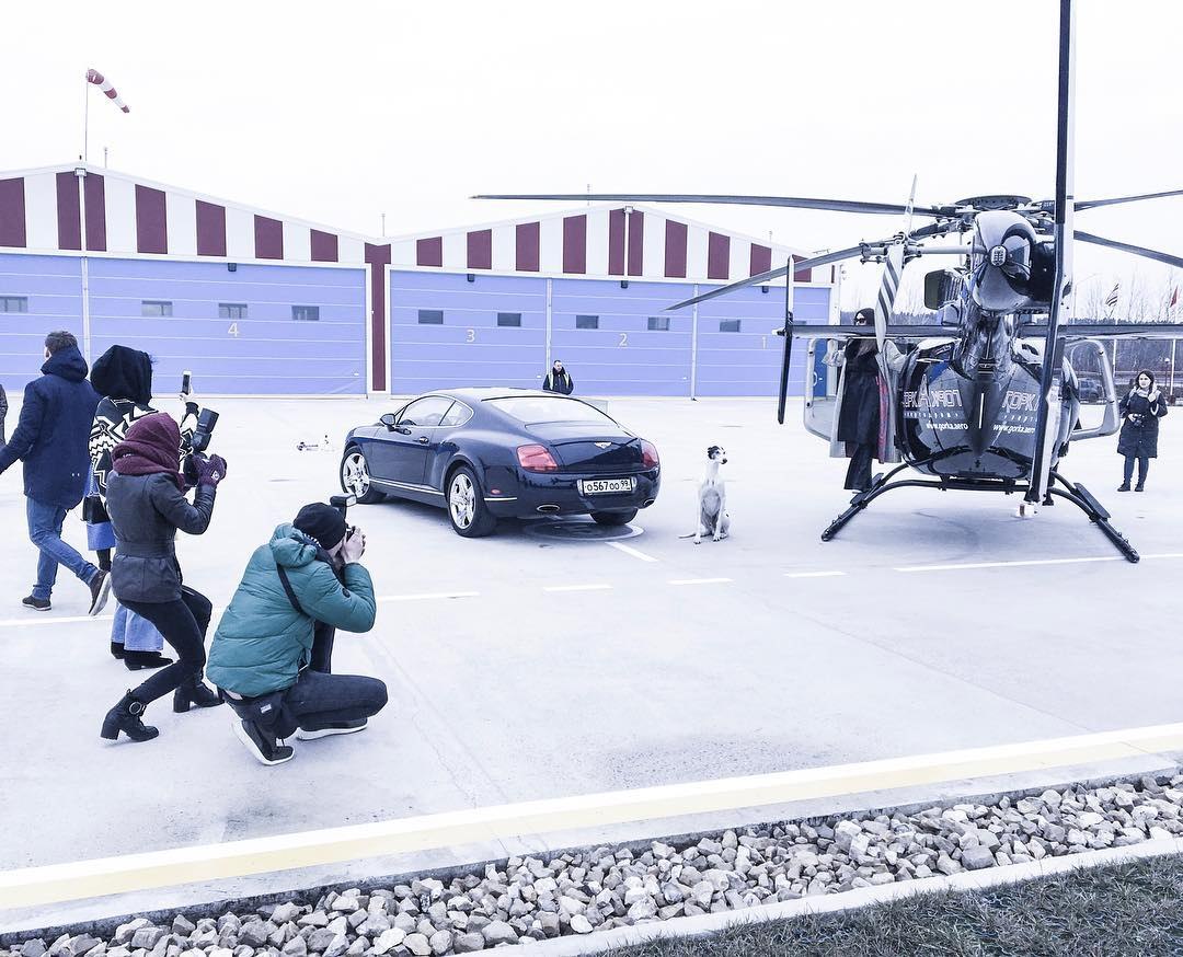 Équipe de tournage en action autour d'un hélicoptère et d'une voiture de prestige